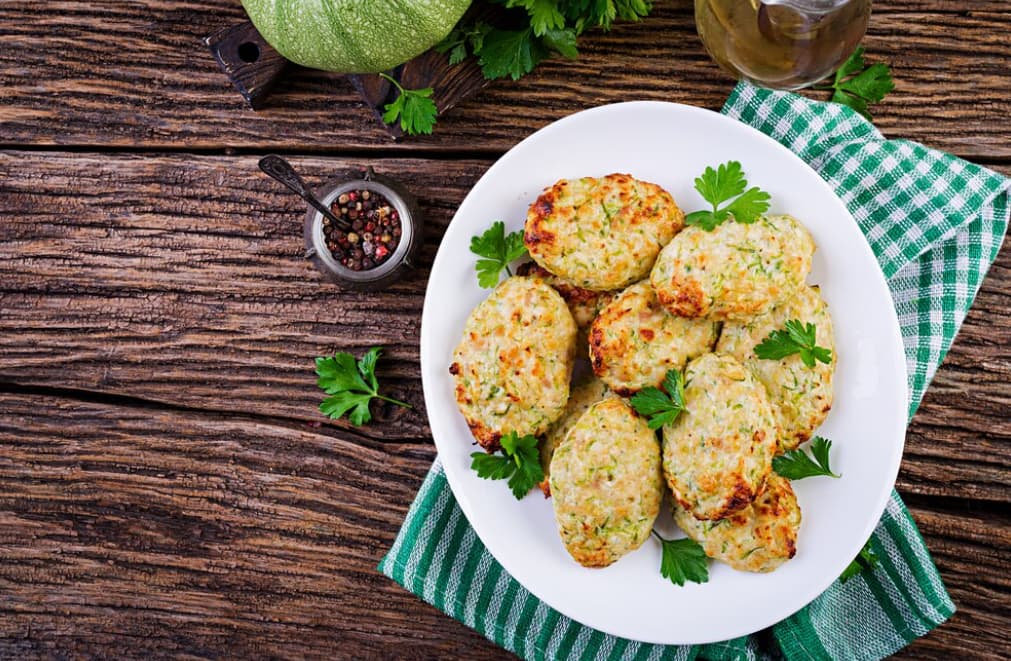 A plate of zucchini fritters garnished with parsley on a wooden table