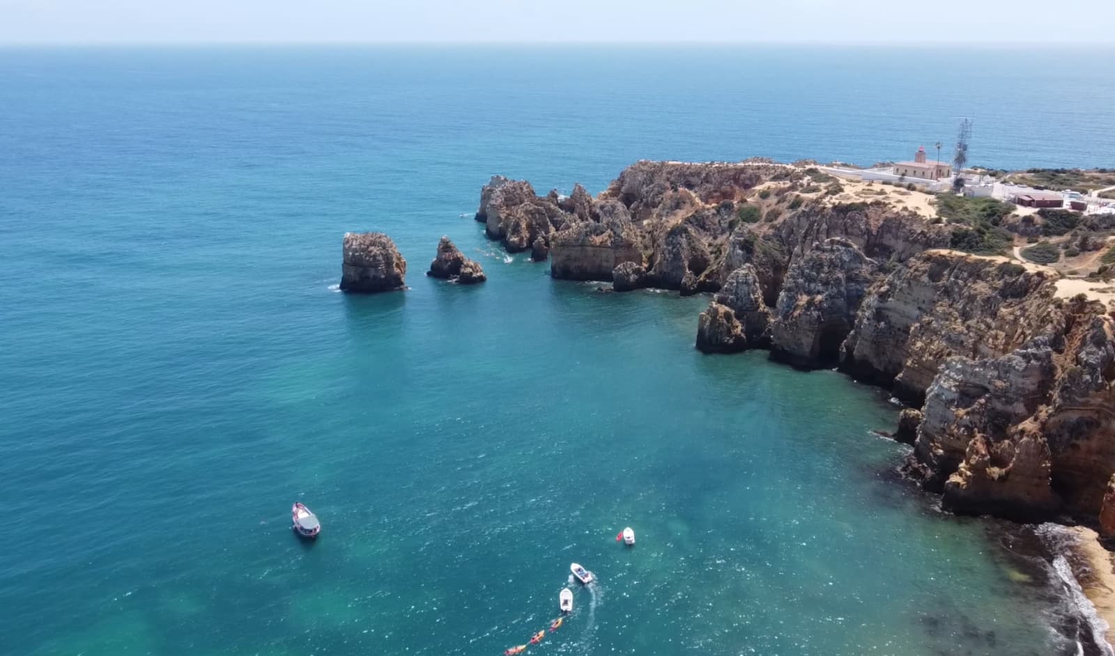 Aerial view of a rugged coastline with sea stacks and a lighthouse