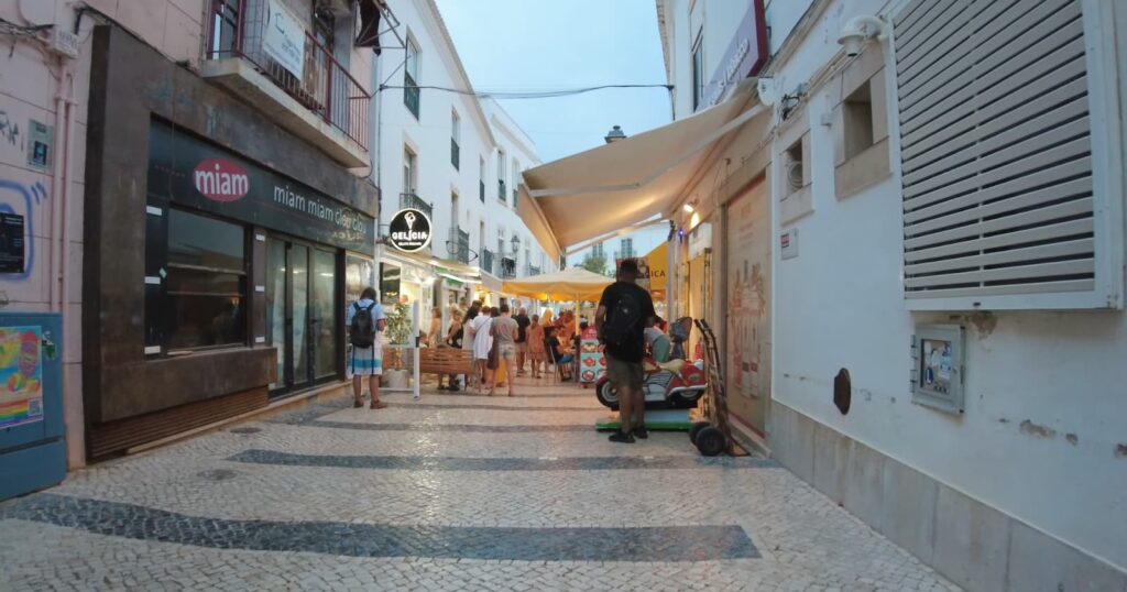 Evening street scene with people, shops, and a scooter in a European town