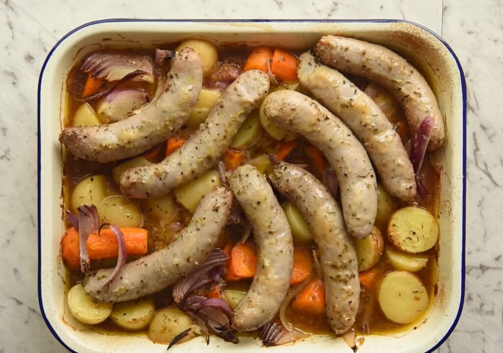 Roasted sausages atop vegetables in a baking dish